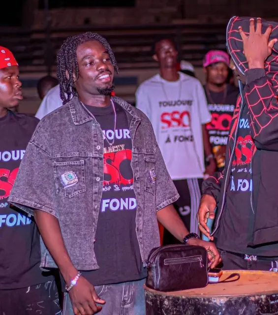 Membre de la team sur scène en veste en jean, foule derrière